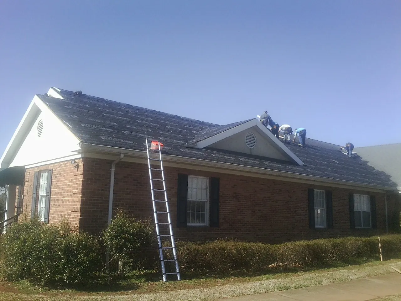 Crew tearing shingles off a brick ranch roof with a ladder set — Emergency Roof Repair work by our crew in Etna Green