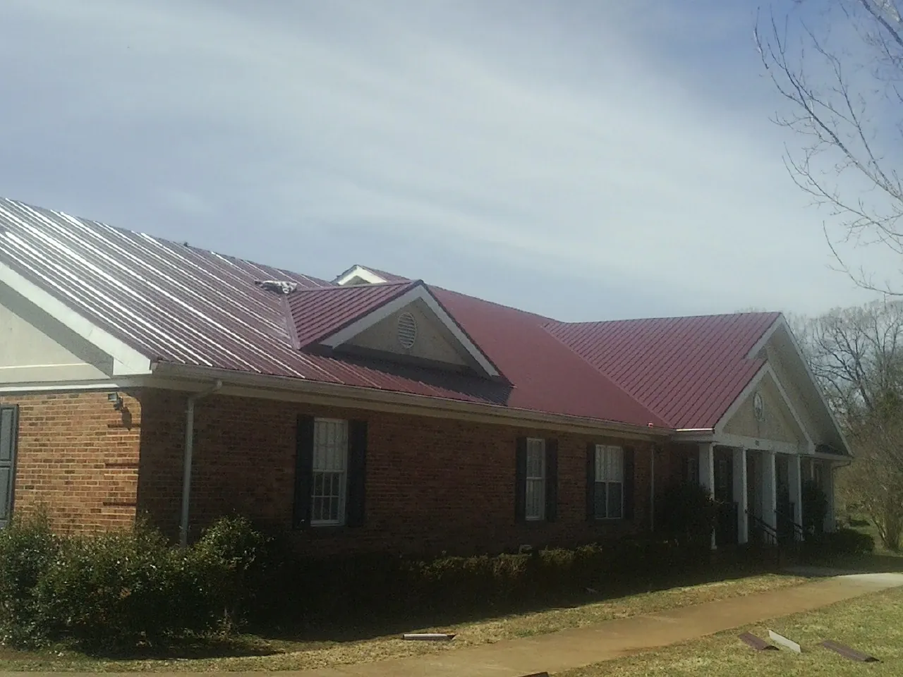 Red metal roof with gabled entries on a long brick building, from a Hail Damage Roof Repair job in Etna Green