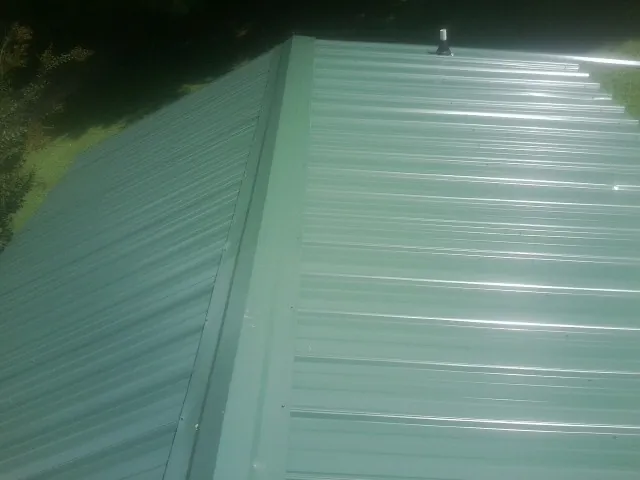 New green metal panels meeting at the ridge of a roof — Flat Roof Repair work by our crew in Etna Green