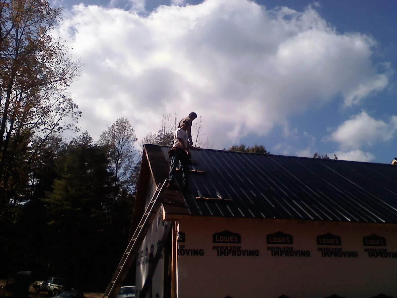 Roofer fastening dark metal panels high against a cloudy sky, from a Roof Inspection job in Etna Green