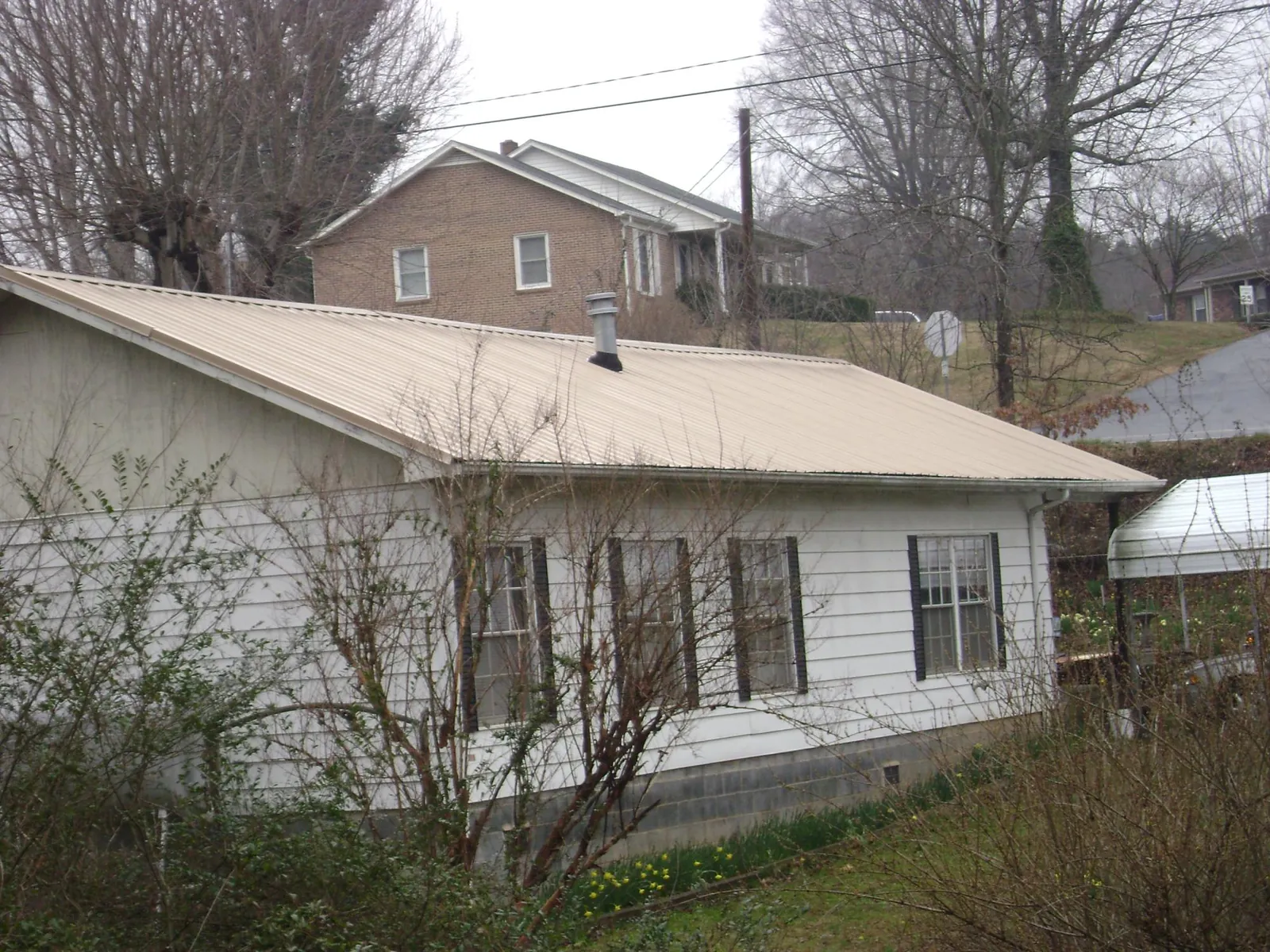 Tan metal roof on a white sided house set into a hillside — Commercial Roofing by Roofing Brothers in Etna Green