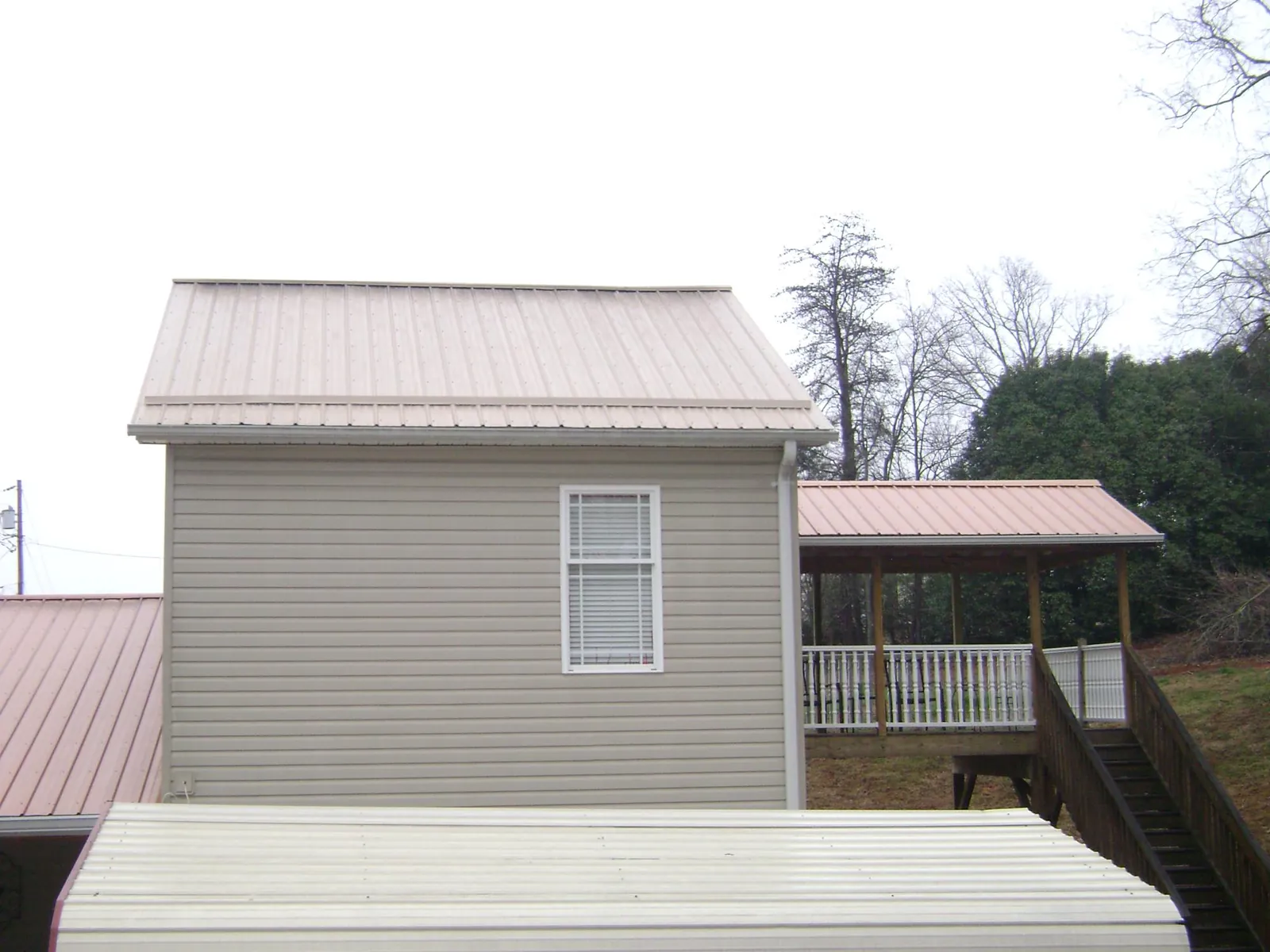 Tan metal roofs on a two story addition and attached porch, from a Roof Replacement job in Etna Green